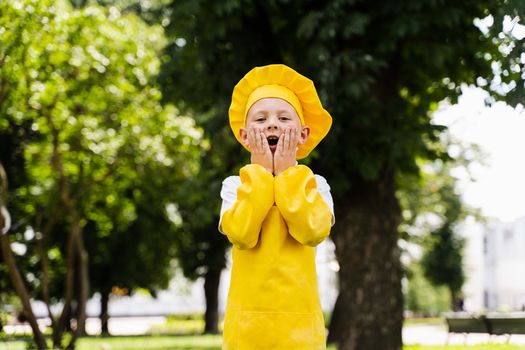 Shocked cook child in yellow chefs hat and apron yellow uniform holding his cheeks and surprise outdoor