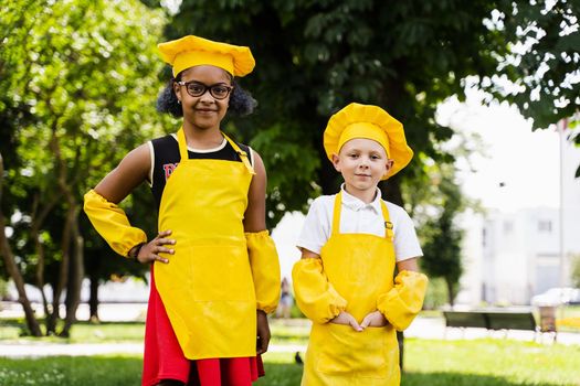 Communication between multiracial friends of black african and caucasian cook children in yellow chefs hat and apron discussing and having fun together