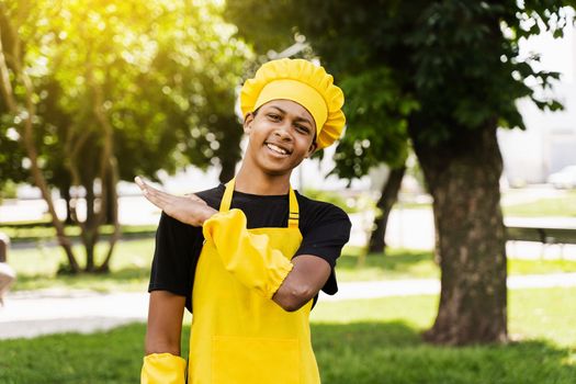 Happy black african teenager cook in chefs hat and yellow apron uniform smiling outdoor. Creative advertising for cafe or restaurant