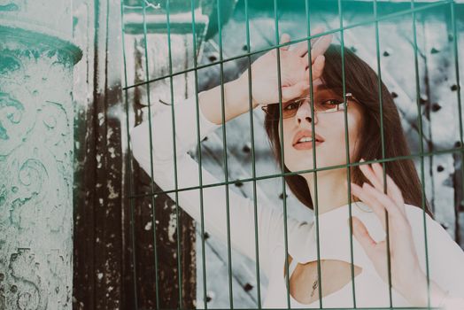 Close-up portrait of woman a in a white blause near a green metal grid