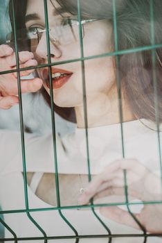 Close-up portrait of woman a in a white blause near a green metal grid