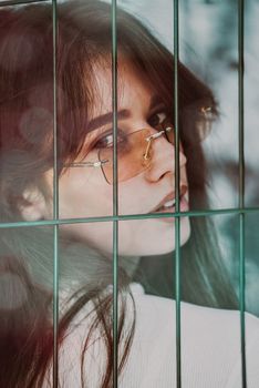 Close-up portrait of woman a in a white blause near a green metal grid