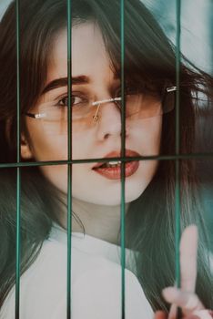 Close-up portrait of woman a in a white blause near a green metal grid