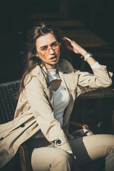 beautiful brunette girl in a sunglasses dressed in white blouse and beige coat. Stylish trendy fashion outlook