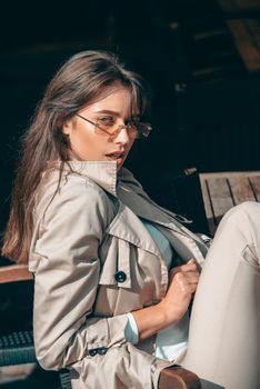 beautiful brunette girl in a sunglasses dressed in white blouse and beige coat. Stylish trendy fashion outlook