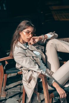 beautiful brunette girl in a sunglasses dressed in white blouse and beige coat. Stylish trendy fashion outlook