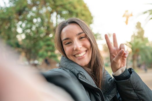Young beautiful woman smiling taking selfie photo at university campus. Trendy girl in casual attire. Positive cheerful female student posing outdoors for sharing in social media app. Caucasian lady