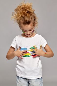 Nice child having a brush in her lovely haircut, wearing in a white t-shirt. She is smearing her t-shirt, on a gray background.