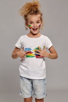 Nice teenager having a brush in her lovely haircut, wearing in a white t-shirt. She is smearing her t-shirt and looking excited on a gray background.