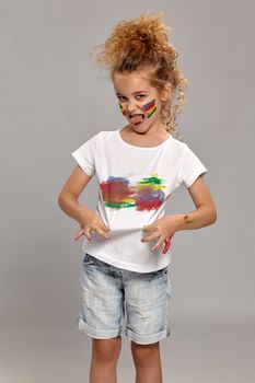 Beautiful little girl having a brush in her lovely haircut, wearing in a white smeared t-shirt and act like she doesnt like it. Loolking at the camera on a gray background.