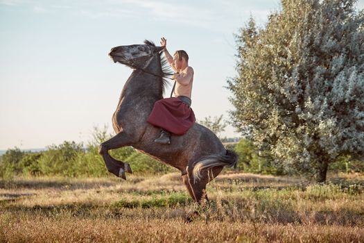 Handsome man cowboy riding on a horse - background of sky and trees. A man in red wide pants without a shirt. Show