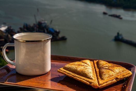 Breakfast - sandwiches and coffee on a wooden tray with natural views.