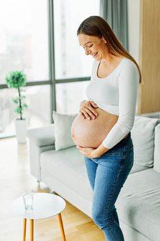 Portrait of a happy young pregnant woman holding her belly at home