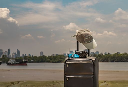 Vacation and travel. Suitcase or luggage bag with Cap, Photo camera and Sun glasses on Pier. Sky, River and Boat in background, Summer vacation holidays traveling design concept. Selective focus.