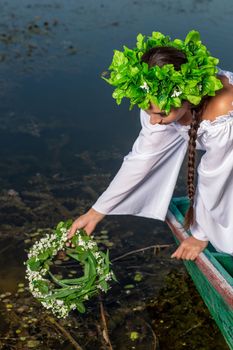 Young sexy woman on boat at sunset. The girl has a flower wreath on her head, relaxing and sailing on river. Beautiful body and face. Fantasy art photography. Concept of female beauty, rest in the village