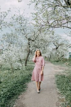 Blonde girl on a spring walk in the garden with cherry blossoms. Female portrait, close-up. A girl in a pink polka dot dress