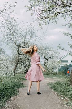 Blonde girl on a spring walk in the garden with cherry blossoms. Female portrait, close-up. A girl in a pink polka dot dress