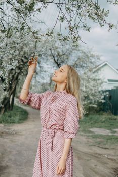 Blonde girl on a spring walk in the garden with cherry blossoms. Female portrait, close-up. A girl in a pink polka dot dress