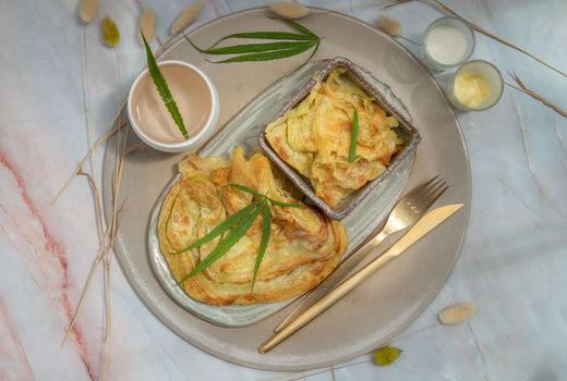 Homemade sweet frying roti (Cannabis Pancake) with Cannabis served with Cannabis tea on ceramic tray. Concept of food with cannabis herb, Treatment of medical marijuana for use in food, Top view, Selective focus.