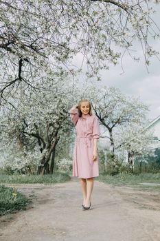 Blonde girl on a spring walk in the garden with cherry blossoms. Female portrait, close-up. A girl in a pink polka dot dress