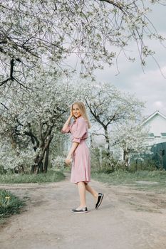 Blonde girl on a spring walk in the garden with cherry blossoms. Female portrait, close-up. A girl in a pink polka dot dress
