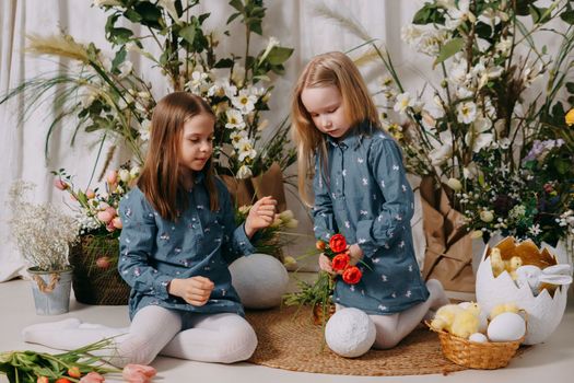 Two girls in a beautiful Easter photo zone with flowers, eggs, chickens and Easter bunnies. Happy Easter holiday