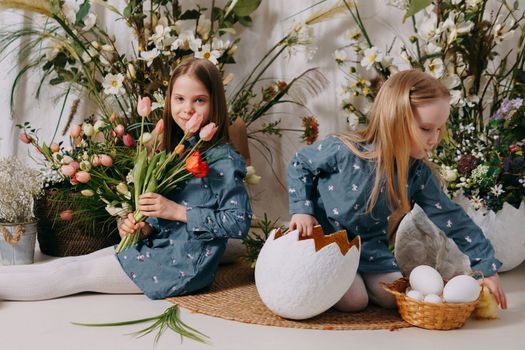 Two girls in a beautiful Easter photo zone with flowers, eggs, chickens and Easter bunnies. Happy Easter holiday