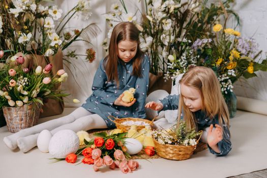 Two girls in a beautiful Easter photo zone with flowers, eggs, chickens and Easter bunnies. Happy Easter holiday