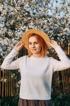 Portrait of a woman in a straw hat in a cherry blossom. Free outdoor recreation, spring blooming garden.