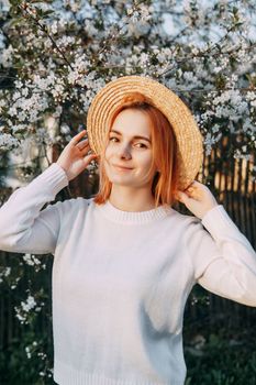 Portrait of a woman in a straw hat in a cherry blossom. Free outdoor recreation, spring blooming garden.