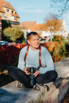 Man Sitting on Stairs in Old European City And Holding Photo Camera. Contemporary Stylish Blogger And Photographer