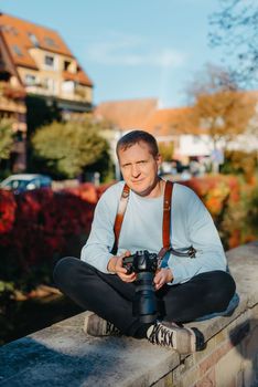 Man Sitting on Stairs in Old European City And Holding Photo Camera. Contemporary Stylish Blogger And Photographer