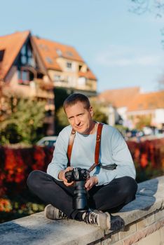 Man Sitting on Stairs in Old European City And Holding Photo Camera. Contemporary Stylish Blogger And Photographer