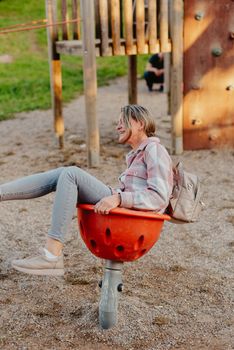 Mother and son having fun on a swing. Motherhood and childhood concept. Sunny summer day. Beautiful family is having fun outside. Parents with children riding on a swing. Mom is playing with her little son on a terrace with swings. A mother woman swings on a swing in the park. Mom and child are on a swing in nature