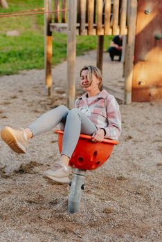 Mother and son having fun on a swing. Motherhood and childhood concept. Sunny summer day. Beautiful family is having fun outside. Parents with children riding on a swing. Mom is playing with her little son on a terrace with swings. A mother woman swings on a swing in the park. Mom and child are on a swing in nature