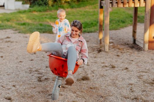 Mother and son having fun on a swing. Motherhood and childhood concept. Sunny summer day. Beautiful family is having fun outside. Parents with children riding on a swing. Mom is playing with her little son on a terrace with swings. A mother woman swings on a swing in the park. Mom and child are on a swing in nature