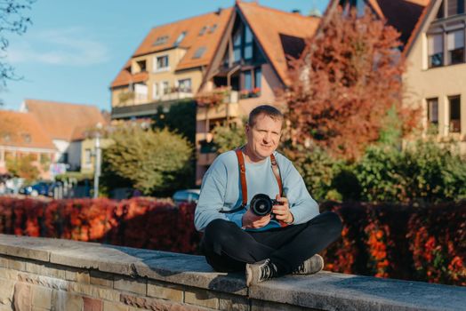 Man Sitting on Stairs in Old European City And Holding Photo Camera. Contemporary Stylish Blogger And Photographer