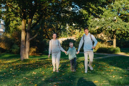 a family mom and 2 sons are having fun, running in the park and jumping. Sons, children, mom, run, play, rejoice, enjoy nature in summer. Family teamwork. Happy family team, running together in field, happily waving their hands. Group of people of different ages. happy family, mom and two sons on an emotional walk. Running and enjoying life in a green field in the park, blue sky, nature.