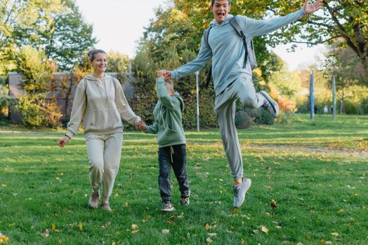 a family mom and 2 sons are having fun, running in the park and jumping. Sons, children, mom, run, play, rejoice, enjoy nature in summer. Family teamwork. Happy family team, running together in field, happily waving their hands. Group of people of different ages. happy family, mom and two sons on an emotional walk. Running and enjoying life in a green field in the park, blue sky, nature.