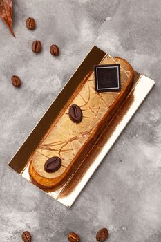 Delicious eclair with coffee flavoured cream filling garnished with chocolate on golden serving cardboard, top view on gray background. Popular French pastry