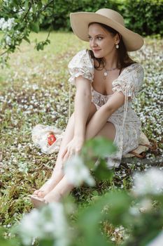 An attractive long-haired woman walks in the spring in the park of blooming apple trees. Spring portrait of a woman