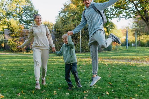 a family mom and 2 sons are having fun, running in the park and jumping. Sons, children, mom, run, play, rejoice, enjoy nature in summer. Family teamwork. Happy family team, running together in field, happily waving their hands. Group of people of different ages. happy family, mom and two sons on an emotional walk. Running and enjoying life in a green field in the park, blue sky, nature.