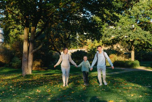 a family mom and 2 sons are having fun, running in the park and jumping. Sons, children, mom, run, play, rejoice, enjoy nature in summer. Family teamwork. Happy family team, running together in field, happily waving their hands. Group of people of different ages. happy family, mom and two sons on an emotional walk. Running and enjoying life in a green field in the park, blue sky, nature.