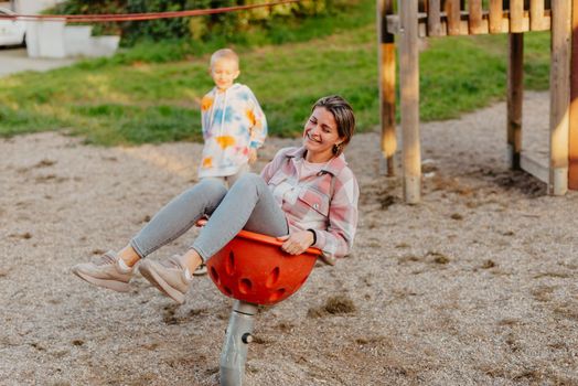 Mother and son having fun on a swing. Motherhood and childhood concept. Sunny summer day. Beautiful family is having fun outside. Parents with children riding on a swing. Mom is playing with her little son on a terrace with swings. A mother woman swings on a swing in the park. Mom and child are on a swing in nature