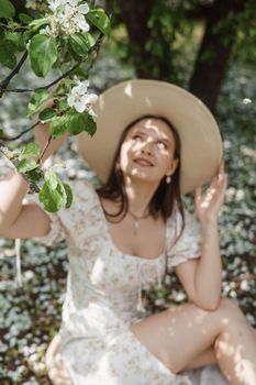 An attractive long-haired woman walks in the spring in the park of blooming apple trees. Spring portrait of a woman