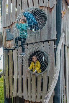 A child climbs up an alpine grid in a park on a playground on a hot summer day. children's playground in a public park, entertainment and recreation for children, mountaineering training. Child playing on outdoor playground. Kids play on school or kindergarten yard. Active kid on colorful slide and swing. Healthy summer activity for children. Little boy climbing outdoors.