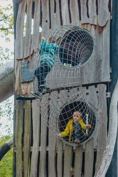 A child climbs up an alpine grid in a park on a playground on a hot summer day. children's playground in a public park, entertainment and recreation for children, mountaineering training. Child playing on outdoor playground. Kids play on school or kindergarten yard. Active kid on colorful slide and swing. Healthy summer activity for children. Little boy climbing outdoors.