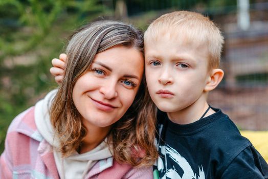 Mother and son outdoor lifestyle portrait in a park setting. Young mother with her seven years old little son are posing. Selective focus. Casual lifestyle photo