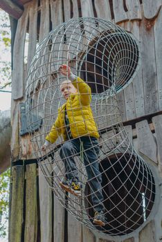 A child climbs up an alpine grid in a park on a playground on a hot summer day. children's playground in a public park, entertainment and recreation for children, mountaineering training. Child playing on outdoor playground. Kids play on school or kindergarten yard. Active kid on colorful slide and swing. Healthy summer activity for children. Little boy climbing outdoors.