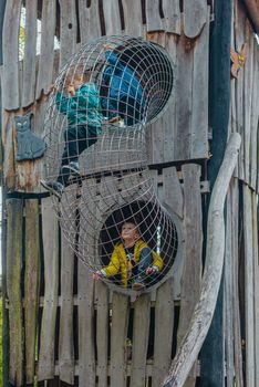 A child climbs up an alpine grid in a park on a playground on a hot summer day. children's playground in a public park, entertainment and recreation for children, mountaineering training. Child playing on outdoor playground. Kids play on school or kindergarten yard. Active kid on colorful slide and swing. Healthy summer activity for children. Little boy climbing outdoors.